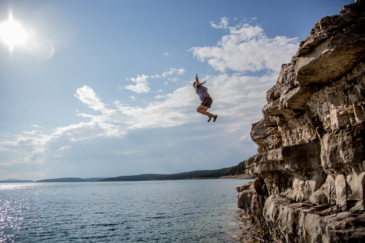 Man jumping off a cliff into a lake