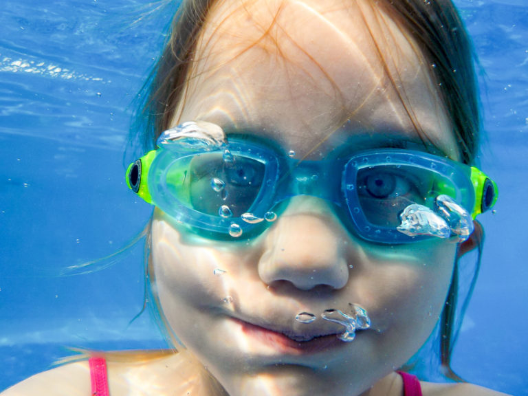 Ein Mädchen mit Taucherbrille taucht im Pool und hält die Luft an