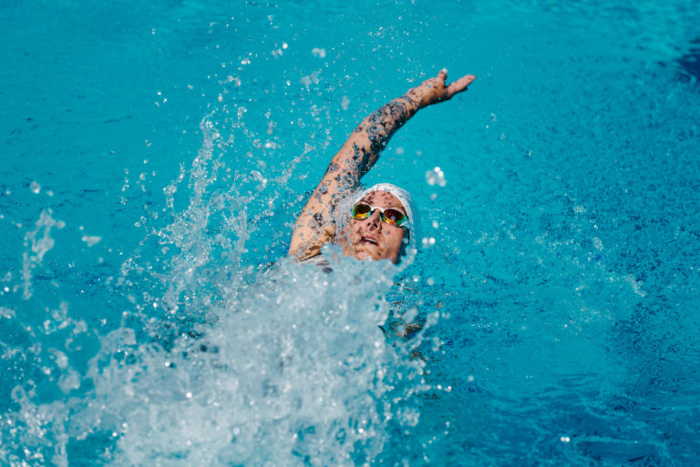 Female with tattoos swimming backstroke