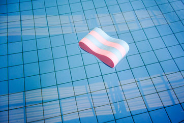 Pink and blue Pull buoy floating abandoned in swimming pool lonely against square tile floor and building silhouette.