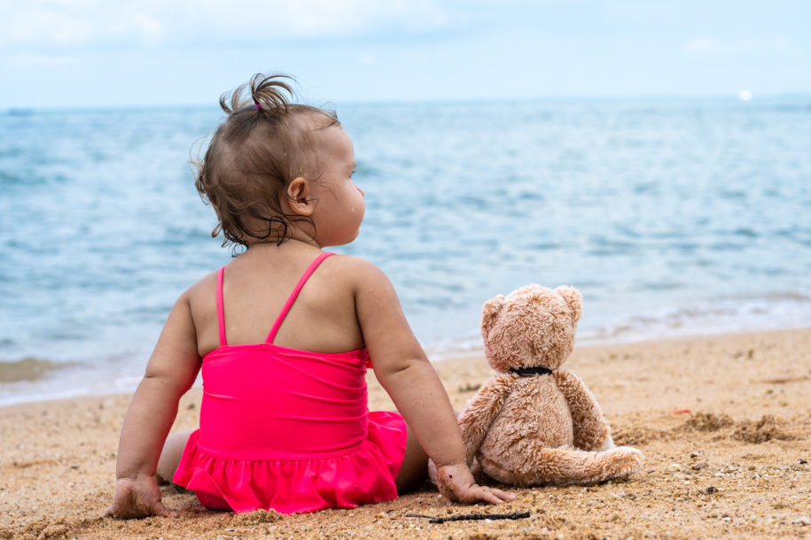 Little girl hugging a teddy bear sitting on the beach. Don't be alone. Sadness and loneliness