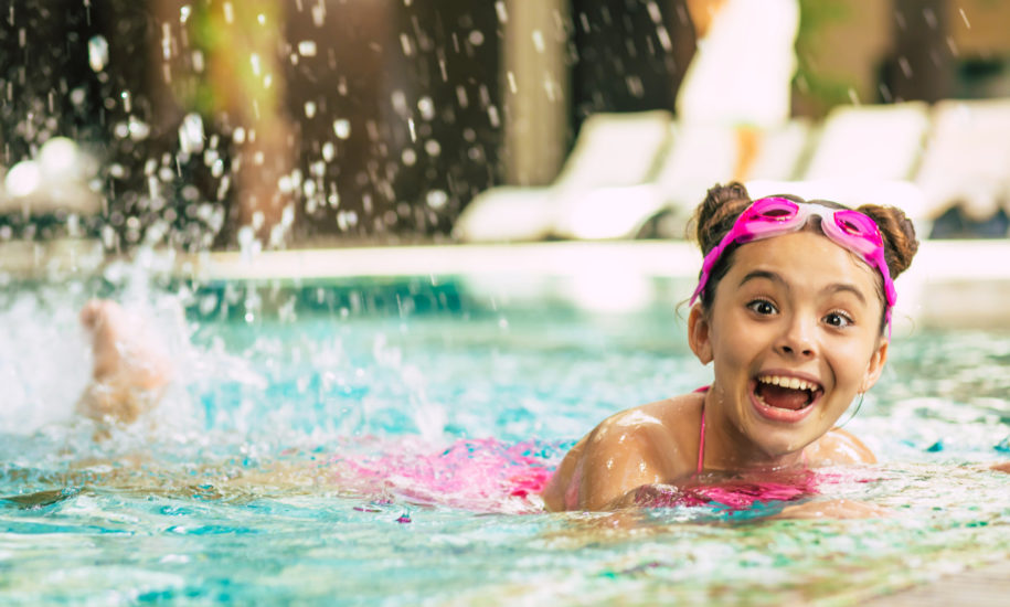 Happy beautiful little smiling girl in goggles and swimsuit in the pool has fun while vacationing or swimming lessons.