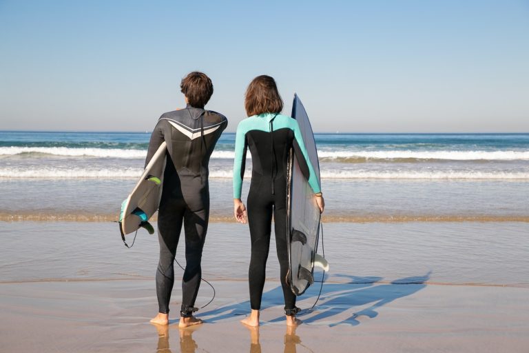 couple holding surfing boards in wetsuit