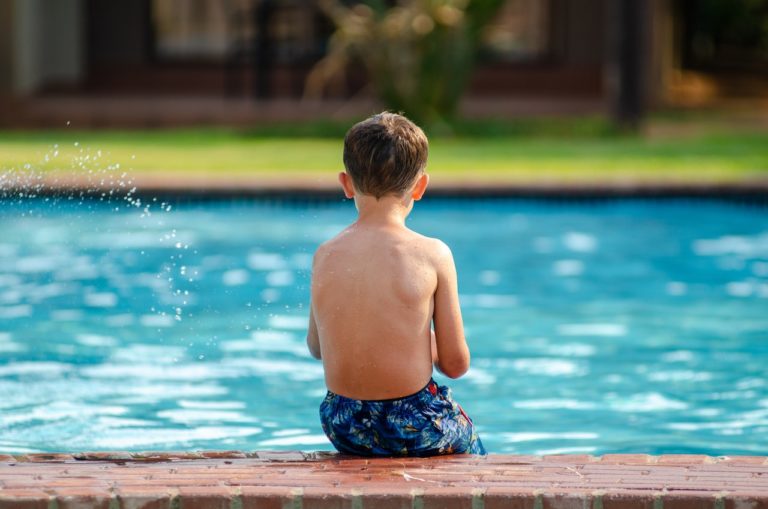 boy in swim shorts sitting on the side of the pool