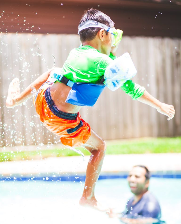boy jumping into pool with neon swimsuit